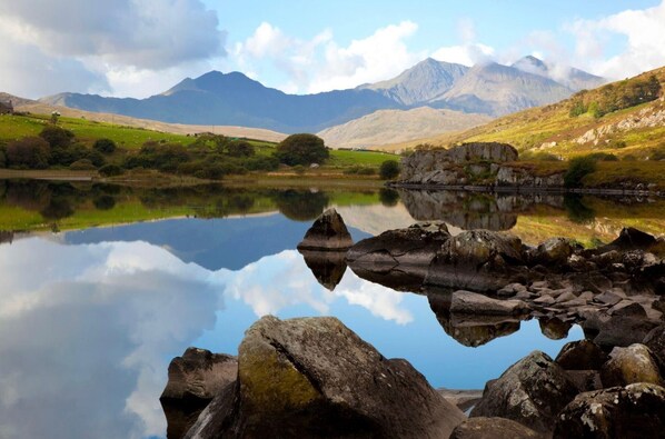 A tranquil lake with clear reflections of the surrounding landscape, including mountains and a small building.