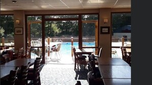 Ein Restaurant mit Außenbereich und Sitzgelegenheiten, das auf einen Swimmingpool mit Blick auf Bäume und einen Zaun blickt.