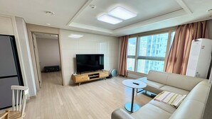 A modern living room with a flat-screen TV, a sofa, a coffee table, and a dining area with a small table and chairs.