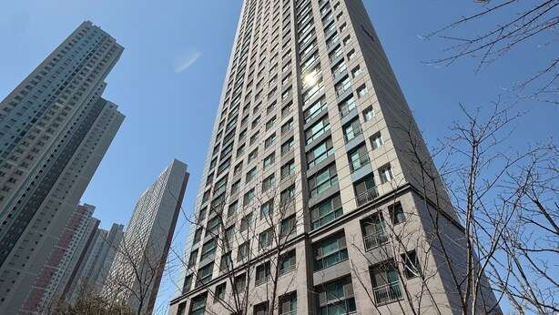 A tall, modern high-rise building with a symmetrical facade, multiple balconies, and a central entrance.