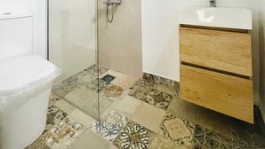 A bathroom with a glass shower enclosure, a white toilet, a wooden vanity with a white sink, and patterned tiles on the floor. - Las Cuevas - 3 bed finca in a serene setting (CN)