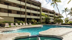 Zona de piscina de hotel con sillones reclinables y un edificio con varios balcones.