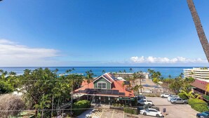 Vista de un edificio con techo rojo y un cartel de Hawaii Family Physicians. Hay un estacionamiento con varios autos y se ve el océano y la playa al fondo.