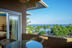 A balcony with a glass door leading to a room, wicker chairs, and a view of the ocean and palm trees. - The Beach Villas w/ Pool Hot Tub & A/C! (Kailua Kona)
