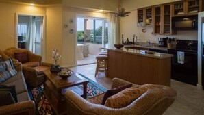 A spacious living area with a sofa, a coffee table, and a dining area with a bar. There is a sliding glass door leading to a balcony. - The Beach Villas w/ Pool Hot Tub & A/C! (Kailua Kona)