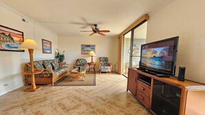 A living room with a television, wicker furniture, and a ceiling fan. - White Sands Village #309 | A/C, Tennis & Pool! (Kailua-Kona)