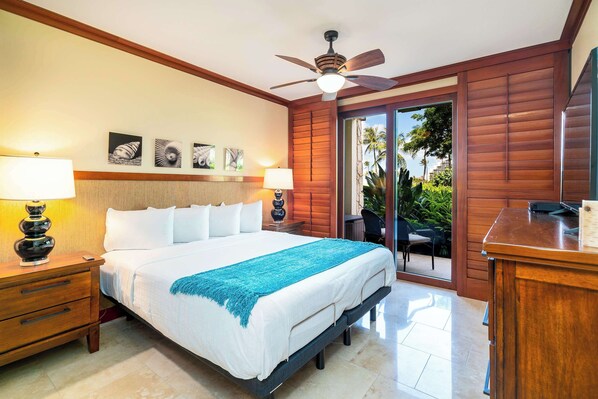 A spacious bedroom with a large bed, wooden headboard, ceiling fan, and a view of the outdoors through a sliding glass door.