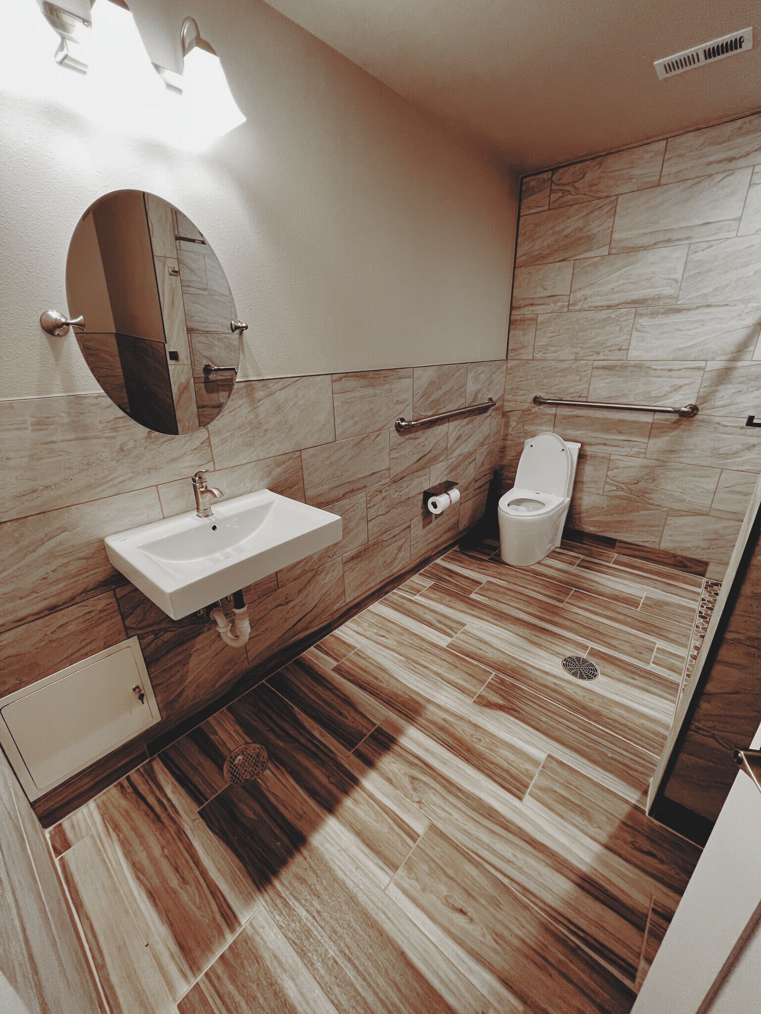 A modern bathroom with a sink, mirror, toilet, and handrails.