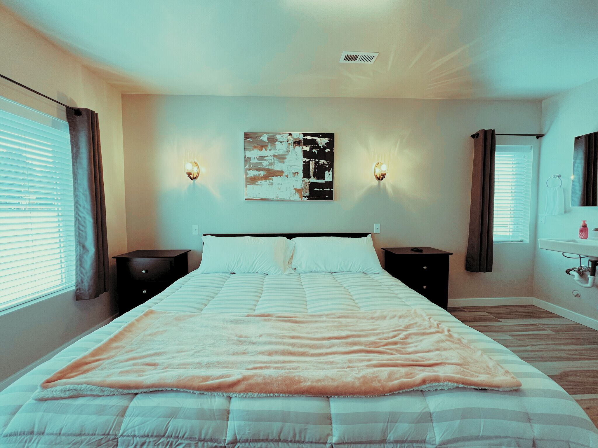 A bedroom with a large bed, two bedside tables, a wall-mounted light fixture, and a window with curtains.