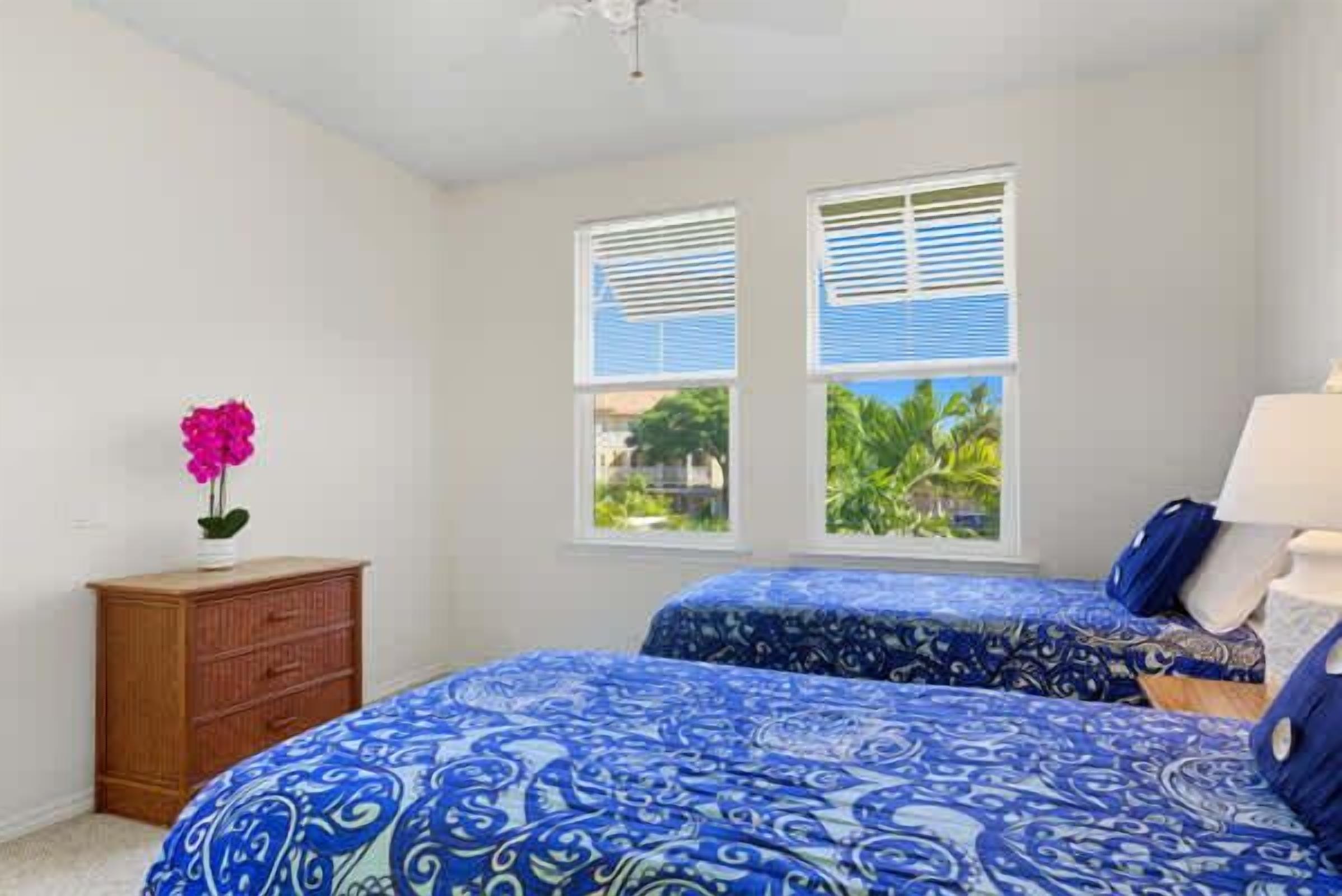 A bedroom with two beds, a wooden dresser, and a window with blinds.