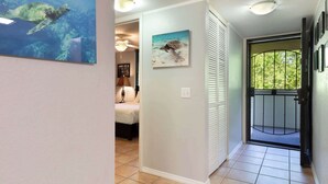 A hallway with a bed, a ceiling fan, and two framed pictures of sea turtles. - Magic Sands Unit 111: Beach and Saltwater Pool (Kailua-Kona)