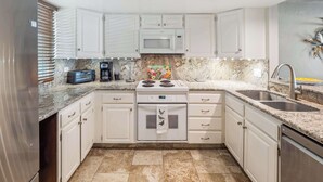 A modern kitchen with white cabinets, a stainless steel refrigerator, a microwave, a stove, a sink, and a coffee maker.