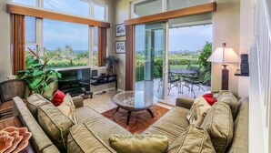 Amplia sala de estar con un sofá grande, una mesa de centro de vidrio y un televisor. Amplias ventanas ofrecen vistas al exterior.