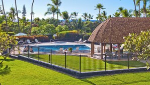 Un área de piscina con sillones de descanso, un pabellón con techo de paja y palmeras.