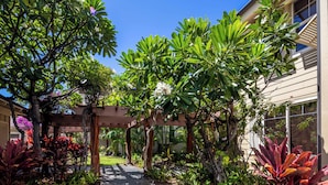 A garden pathway leading to a wooden pergola with lush greenery and flowering plants. - Hale Laki – Stunning Resort Condo, Close to Beach! (Waikoloa)