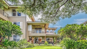 A two-story house with a covered patio, a well-maintained lawn, and various plants. - Hale Laki – Stunning Resort Condo, Close to Beach! (Waikoloa)