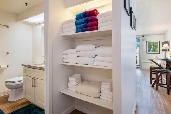A bathroom with a toilet, sink, and shelves with folded towels. - Marine Surf Waikiki w/ Beach Gear & Parking! (Honolulu)