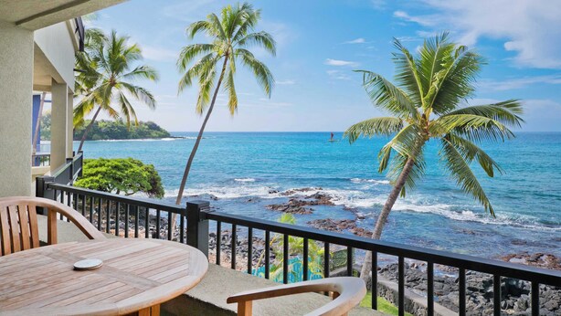 Ein Balkon mit Blick auf das Meer, Palmen und einem Tisch mit Stühlen.