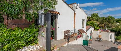 Un edificio blanco con una puerta verde, una escalera y un pequeño espacio al aire libre con sillas y una mesa.