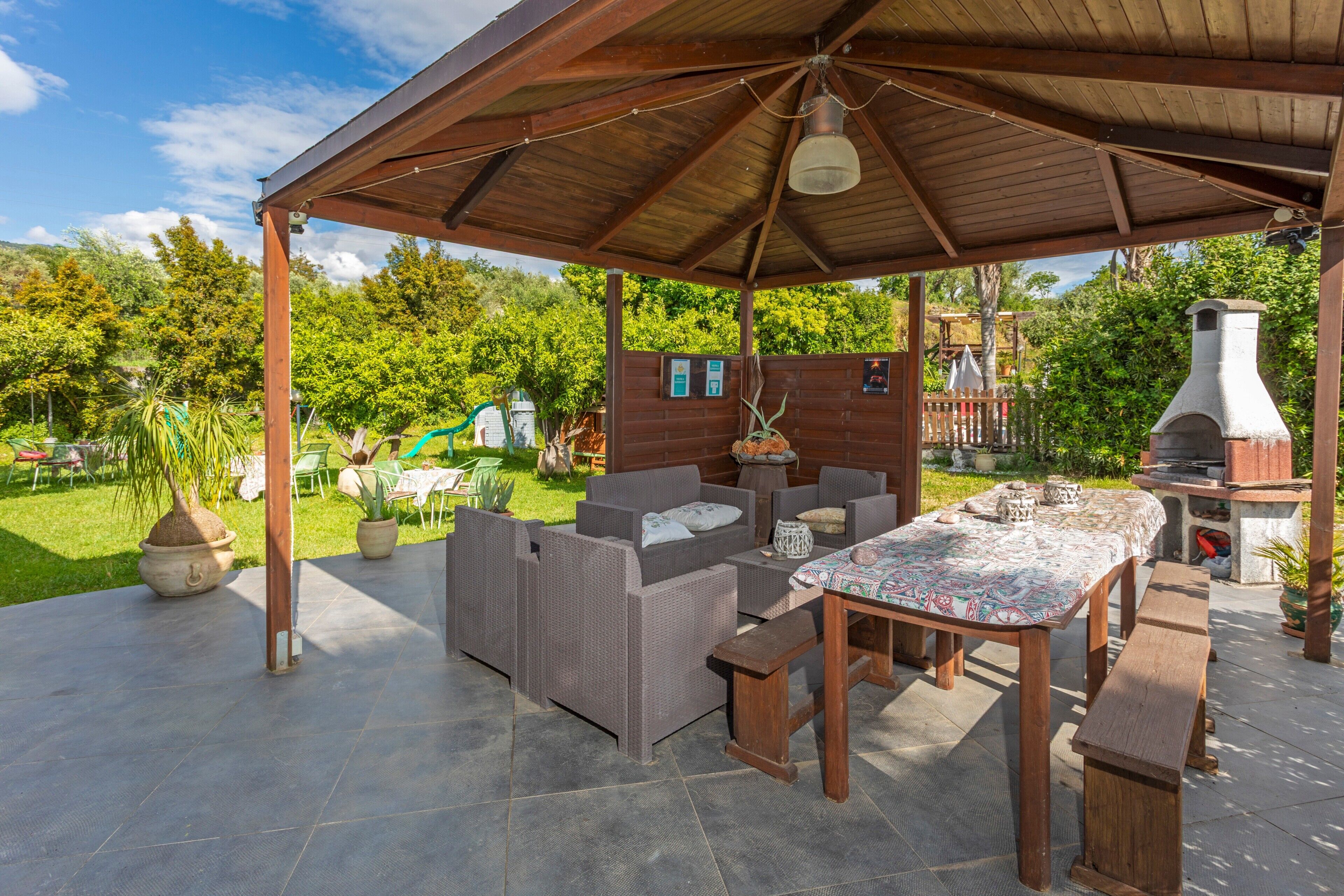 Un patio al aire libre con muebles de mimbre, una mesa con mantel estampado y piso de baldosas de piedra.