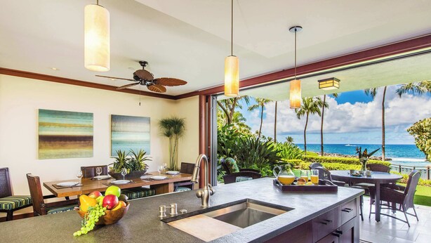 A modern kitchen with a large island, a dining area with a view of the ocean, and a ceiling fan.