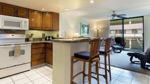 Cocina con armarios de madera, estufa blanca y microondas. Cuenta con una barra con dos taburetes y vistas al balcón.