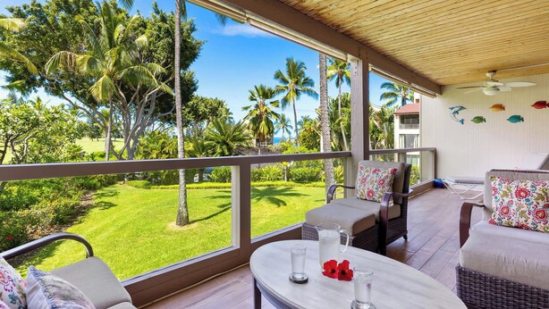 A spacious balcony with a view of a lush garden and palm trees.
