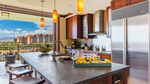 A modern kitchen with a large island, stainless steel appliances, and a view of a cityscape. - Hale Leilani | Ko Olina |  Beachfront w/ Views! (Kapolei)