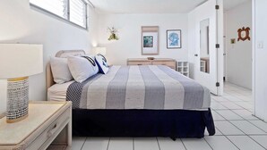 A bedroom with a bed, bedside table, lamp, and wall decorations. - Kolu Honu at Kona Ali'i- Stunning Beachfront Condo (Kailua-Kona)