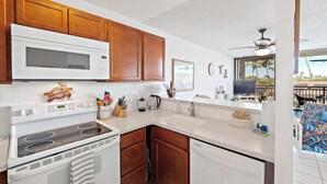 A modern kitchen with wooden cabinets, a microwave, stove, and dishwasher. - Kolu Honu at Kona Ali'i- Stunning Beachfront Condo (Kailua-Kona)