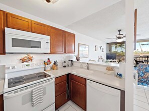Keittiössä on valkoiset kodinkoneet, puukehikot ja sieltä on näkymä ulos.