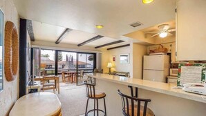 A kitchen with a bar area, wooden stools, a refrigerator, and a ceiling fan.