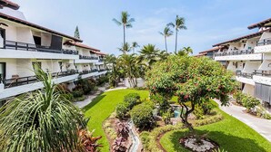 A hotel courtyard with a central garden, palm trees, and a large tree with red flowers.