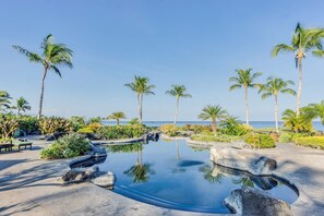 A serene pool area with palm trees and a clear view of the ocean.