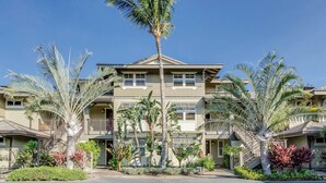 A multi-story hotel with balconies, palm trees, and a well-maintained garden.
