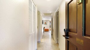 Un couloir d’hôtel avec une porte en bois, un mur blanc avec une fenêtre et un sol de couleur beige.