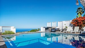 Une piscine d’un bleu éclatant, avec vue sur l’océan, entourée de panneaux en treillis blancs et de chaises longues.