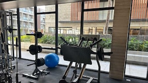 A gym with exercise equipment, a blue exercise ball, and large windows offering views of buildings and greenery.