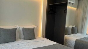 A hotel room with two beds, a wardrobe, and an air conditioning unit.