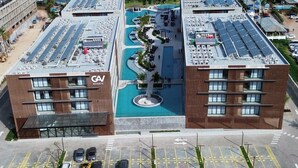A hotel with a rooftop pool, a parking lot, and a view of the ocean.