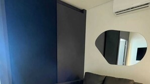 A modern room with a dark-colored sofa, a large mirror, and a wall-mounted air conditioner.