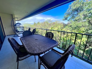 Enjoy a tranquil view of lush greenery from this balcony with a table and chairs.