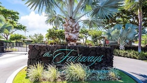 Uma placa de pedra com a inscrição 'the Fairways', rodeada por plantas tropicais e palmeiras.