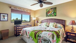 A bedroom with a bed, a ceiling fan, a TV, a window with a view, a painting, and a lamp.