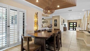 A spacious dining area with a wooden table and chairs, a decorative light fixture, and a view of the outdoors through sliding glass doors. - Hale Nene | Pool, Hot Tub & Ocean Views! (Kailua Kona)