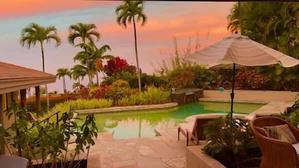 A pool area with lounge chairs and umbrellas, surrounded by palm trees and a sunset sky. - Hale Nene | Pool, Hot Tub & Ocean Views! (Kailua Kona)