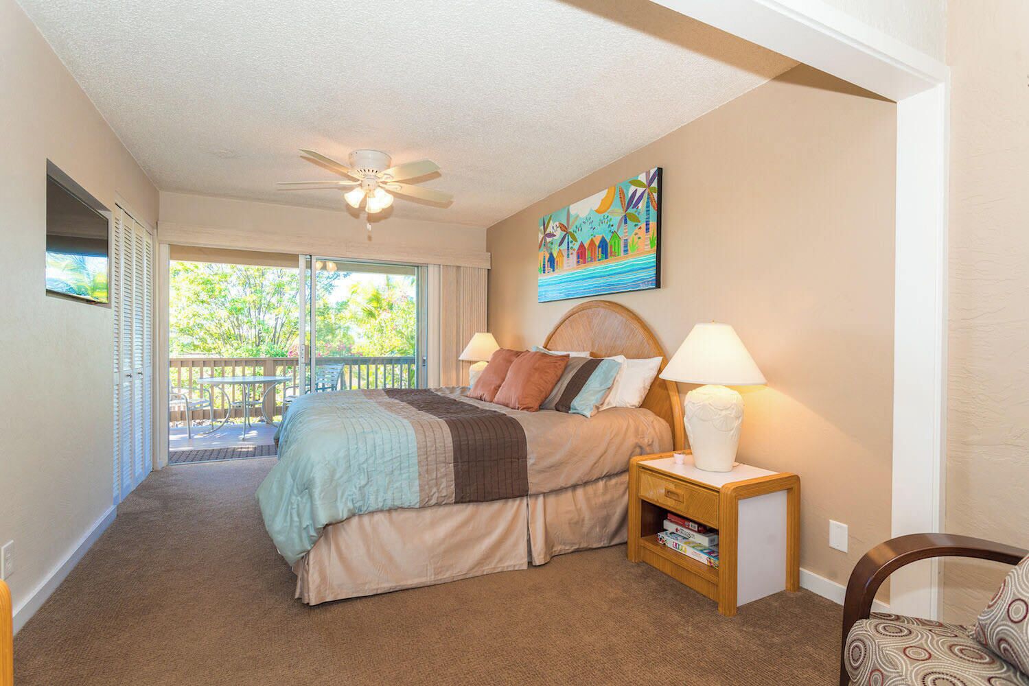 Una camera da letto con un letto, un comodino, una ventola a soffitto, un quadro e vista sull'esterno.