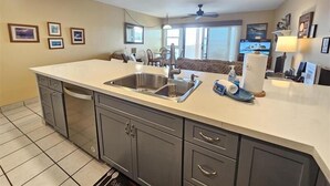 Una cocina moderna con una isla grande, pileta de acero inoxidable y muebles grises.