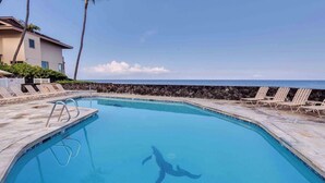 Una piscina azul y transparente con una silla de salvavidas, sillas de descanso y vista al océano.