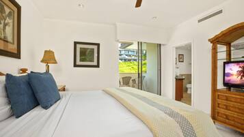 A bedroom with a bed, a ceiling fan, a TV, and a balcony with a view of buildings and greenery.